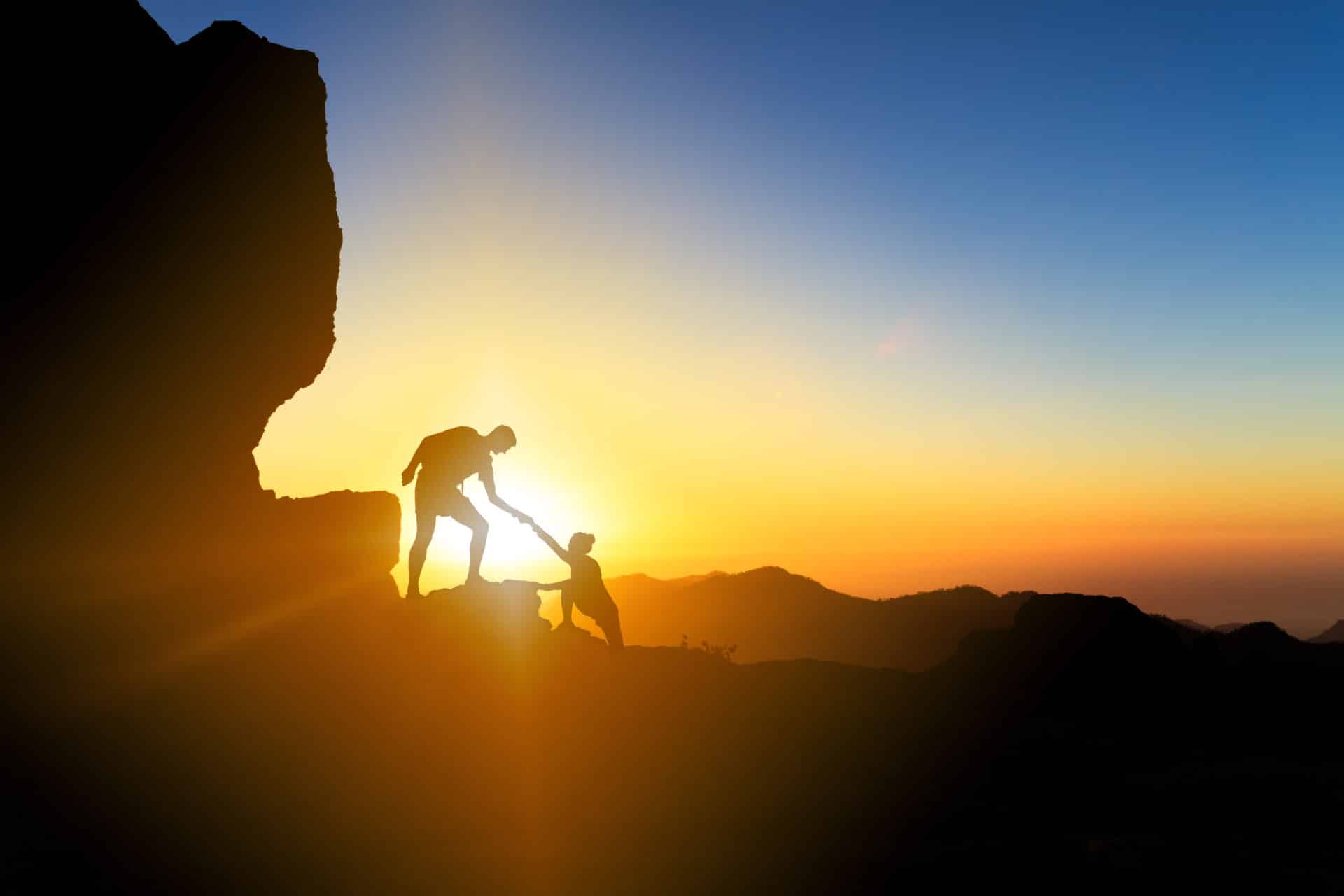 A woman's recovery coach helping her climb up a mountain during sunrise
