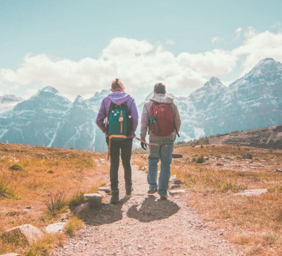 A person in recovery with his sober coach walking on a mountain trail towards snowy mountains